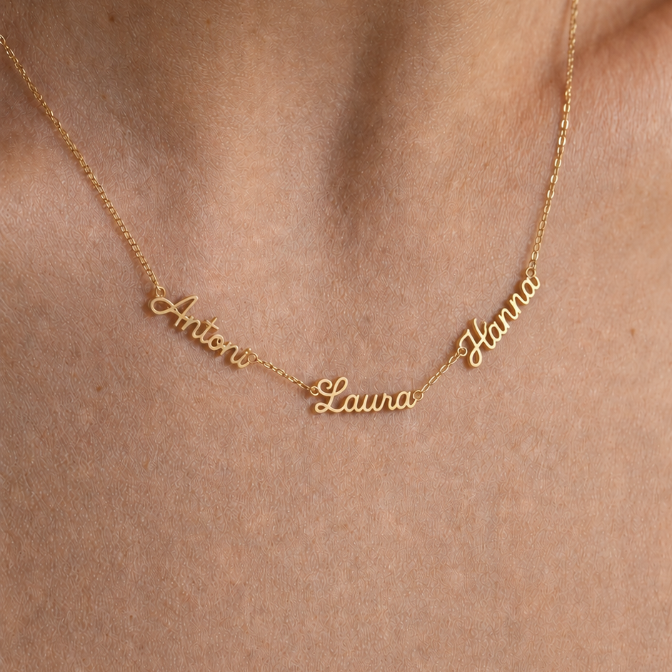 A close-up of a gold chain necklace worn on a person's neck, featuring personalized script names 'Antonio', 'Laura', and 'Hanna'.