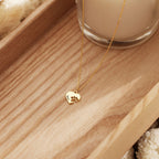 A gold chain necklace with a small heart-shaped pendant featuring a paw print and the name 'Mochi', displayed on a wooden tray next to a glass candle.