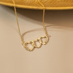 Gold family name necklace with three name hearts, styled on a soft beige background next to a gold tray.