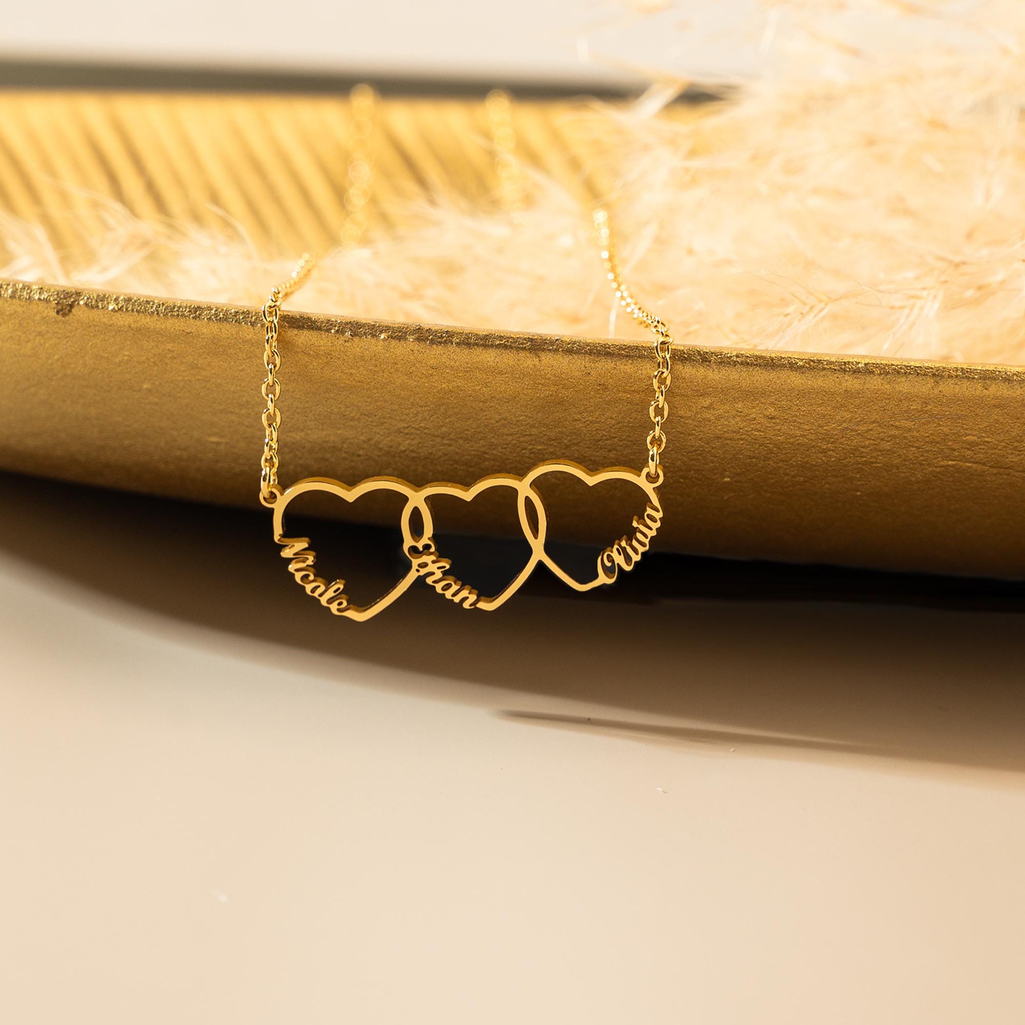 Detail shot of the three interlocking hearts, each cut around a name in handwritten script, in gold plating.