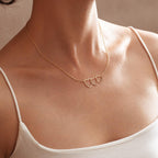 Delicate gold three-heart name necklace worn at collarbone length with a white strap top.