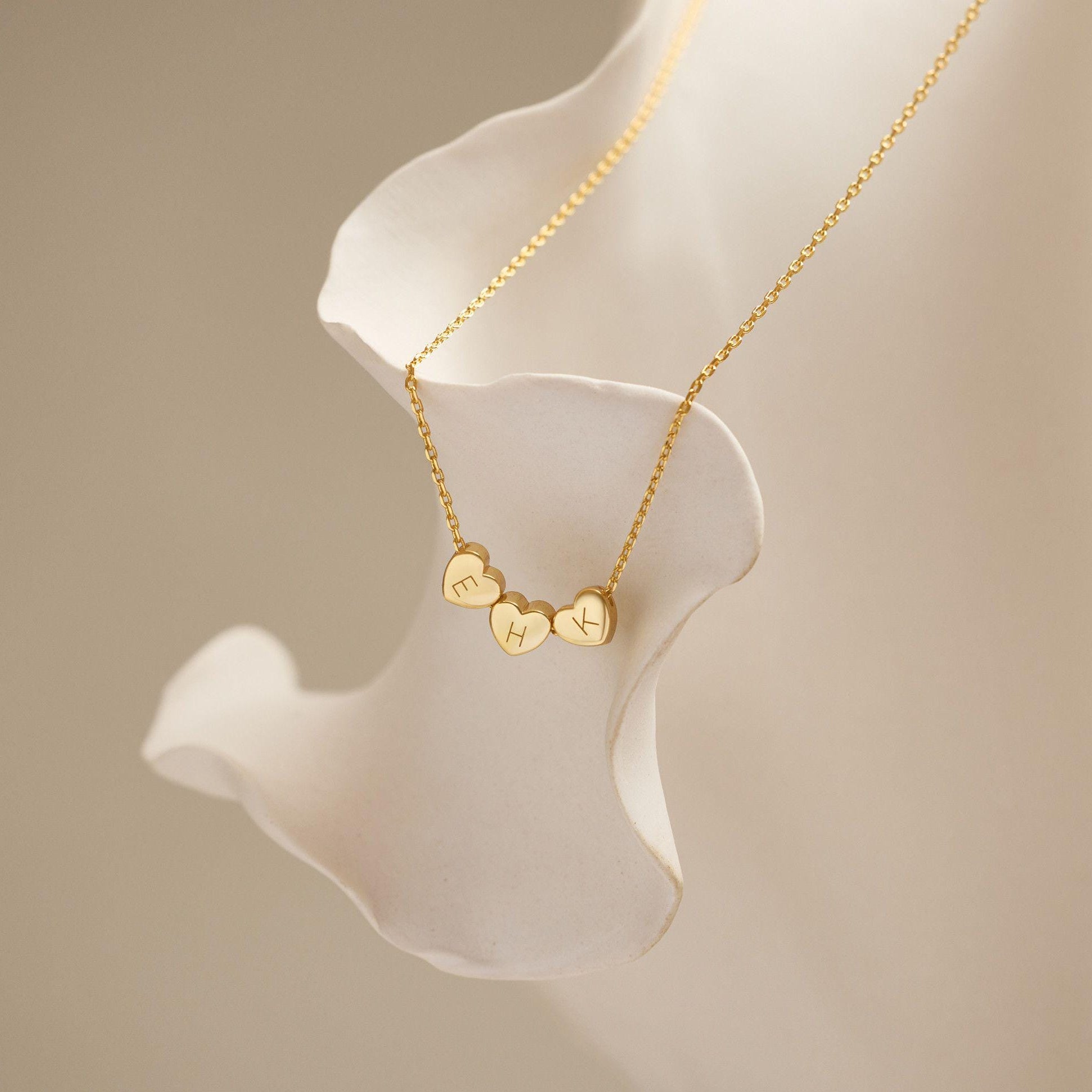 Gold necklace with heart-shaped pendants on a white mannequin bust against a beige background