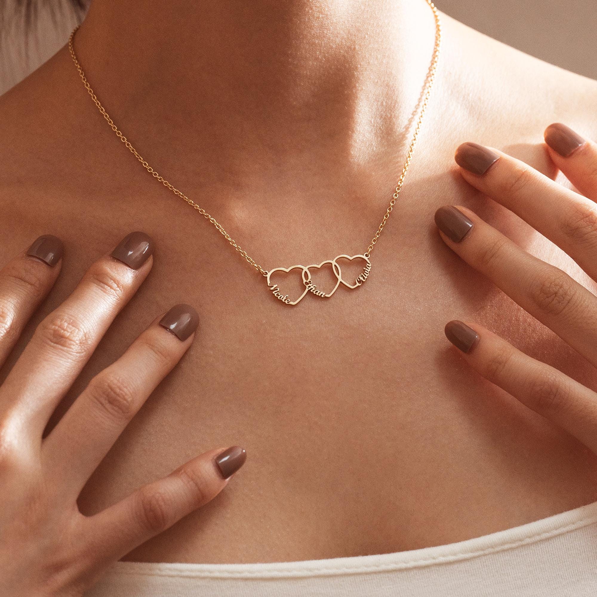 Woman wearing a gold family name necklace with three interlocking name hearts resting just below the collarbone.