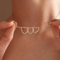 Close-up of a gold family name necklace with three interlocking open hearts, each shaped around a child's name, held up against a woman's neck.