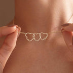 Close-up of a gold family name necklace with three interlocking open hearts, each shaped around a child's name, held up against a woman's neck.
